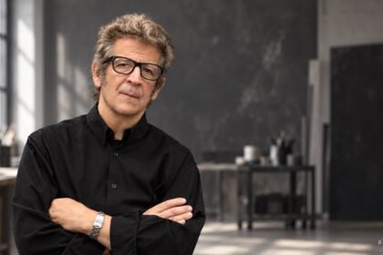 Robert Longo mit schwarzer Brille vor einem künstlerisch gestalteten Atelierhintergrund